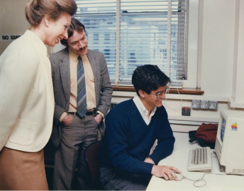Three people around an old computer. One of them is Princess Anne. It is the eighties.