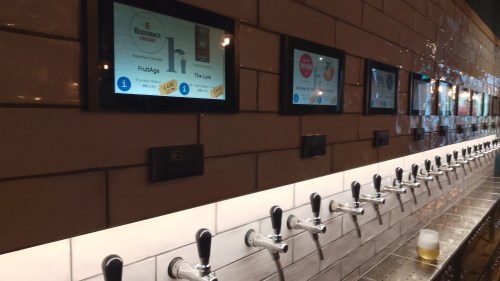 Interior of the Tap House, Nottingham. A wall of self-service beer taps along a wall, each with a small screen above