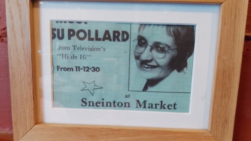 A framed advert announcing Su Pollard is making an appearance at Sneinton Market. It looks quite old.
