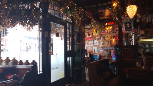 Interior of the Tamworth Tap, there are hops and fairy lights hanging from the ceiling, lots of old Belgian beer ads on the walls and wooden pews as seating