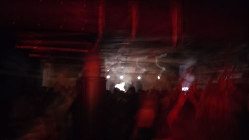 A blurry photo from the back of a gig, there are lots of people in front of the stage, a figure on the stage appears to glow white